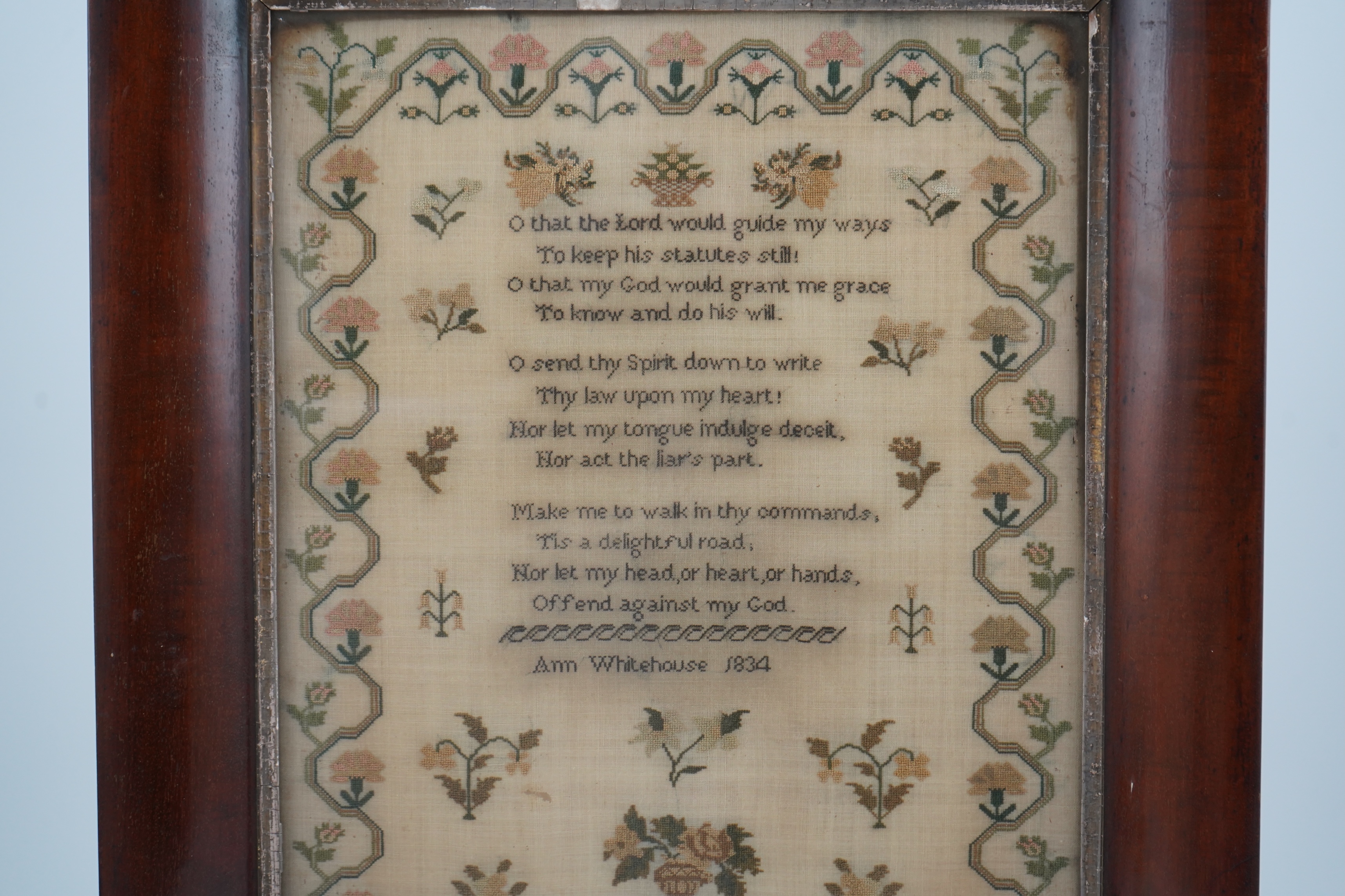 A wide mahogany framed sampler by Ann Whitehouse dated 1834, worked in coloured silks on a fine linen ground, in small stitches, bordered with a geometric stylistic vining pattern, set with a central verse, above her nam